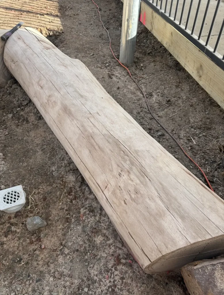 A dressed hardwood log on site beside a fence, ready to use as a landscape feature